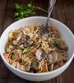 a white bowl filled with pasta and clams on top of a wooden table next to a fork