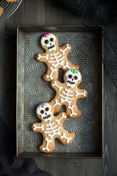 two decorated sugar cookies in the shape of skeletons on a metal tray next to plates