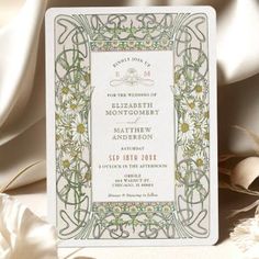 a wedding card with an ornate design on the front and back, sitting next to some flowers