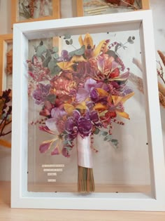 a vase filled with purple flowers sitting inside of a white framed display case on top of a wooden table