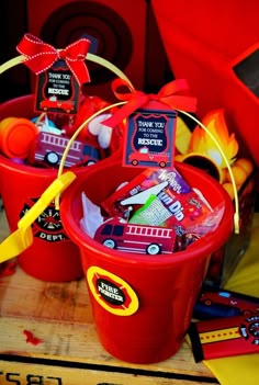 two red buckets filled with candy sitting on top of a wooden table next to other items