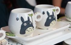 three coffee cups with totoro designs on them are sitting on a tray in front of two people