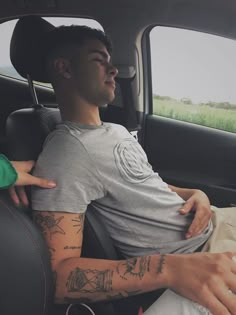 a man sitting in the back seat of a car with tattoos on his arm