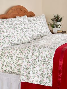 a bed with white and red sheets on it next to a potted plant in the corner