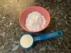 a pink bowl filled with white powder next to a measuring spoon on a granite counter