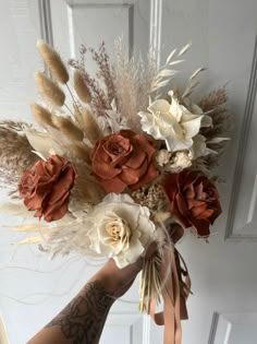 a hand holding a bouquet of flowers in front of a white door with brown ribbon