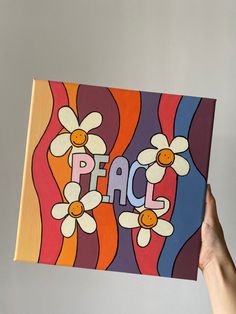 a person holding up a piece of art with the word peace painted on it and daisies