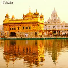 the golden building is reflected in the water near other white buildings and people walking around it