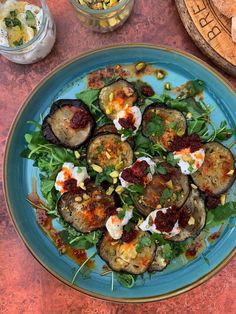 a blue plate topped with eggplant and spinach salad on top of a table