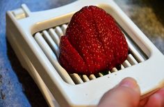 a person is holding a red strawberry in a white strainer on a blue surface