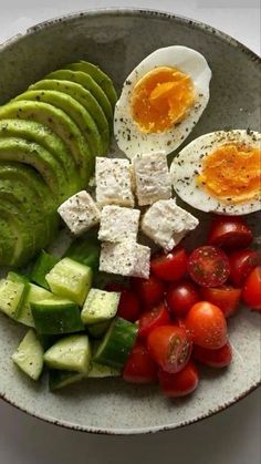 a bowl filled with eggs, cucumber, tomatoes and other foodstuffs