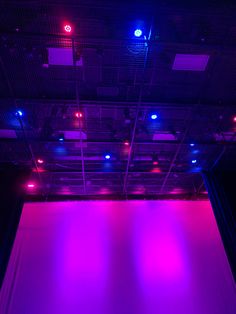 an empty stage lit up with purple lighting and blue lights on the ceiling, in front of a black background