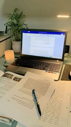 an open laptop computer sitting on top of a desk next to a pen and paper