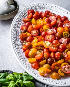 a white plate topped with lots of different types of tomatoes next to some basil leaves