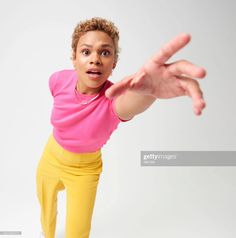 a woman in pink shirt and yellow pants making a hand gesture