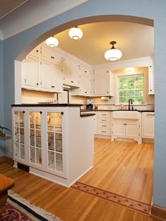 an archway in the middle of a kitchen with white cabinets and wood flooring, along with hardwood floors