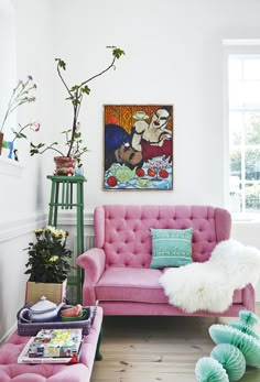 a living room with pink couches and plants in the corner, along with pictures on the wall