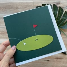 a hand holding up a card with a golf ball on it and a hole in the middle