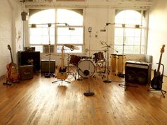 a room filled with lots of musical instruments on top of a hard wood floor next to windows