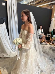 a woman in a wedding dress standing next to a white bouquet