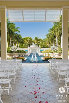 an outdoor wedding venue with white chairs and rose petals on the ground in front of a fountain