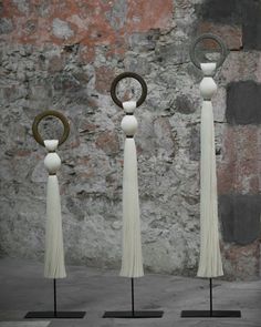 three sculptures with tassels on stands in front of a stone wall and brick wall