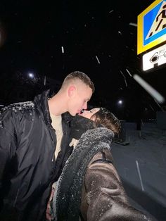 a man and woman kissing in the snow at night with an atm sign behind them