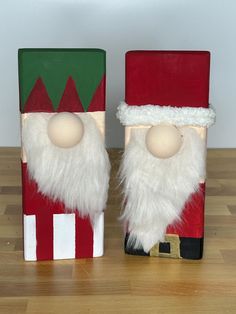 two wooden santa clauss sitting next to each other on a wood floor in front of a white wall