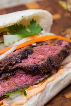 a steak sandwich with lettuce, carrots and mayonnaise on a cutting board