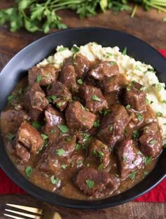 meat and gravy on mashed potatoes in a black bowl with garnish