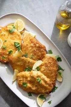 two fried fish fillets on a plate with lemon slices and parsley