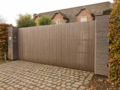 a brick driveway with a wooden fence in front of it and some bushes on the other side