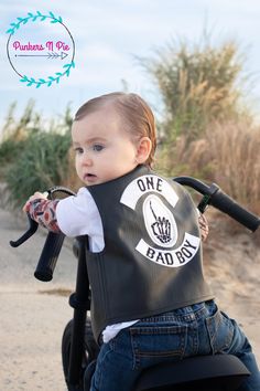 a young child wearing a black leather vest with the words one bad boy on it