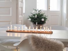 a white dining room table and chairs with candles on the long wooden tray in front of it