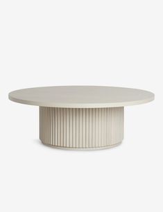 a round table with pleated edges and a circular base in white marble, on a grey background