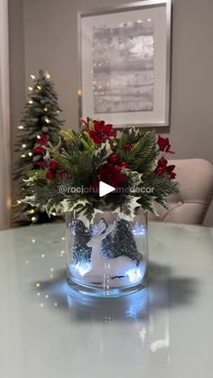 a glass vase filled with red flowers and greenery on top of a white table