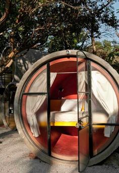 a round bed in the middle of a tree filled area with white sheets on it