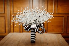 a black and white striped vase with flowers in it sitting on a table next to a wooden paneled wall