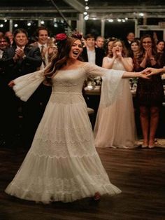 a woman in a white dress is dancing with her arms out and people are standing behind her