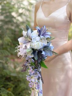 a woman in a dress holding a bouquet of flowers and greenery with her hand