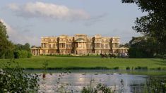 a large house sitting on top of a lush green field next to a lake in front of it