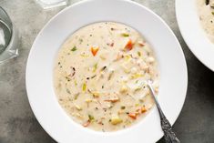 two white bowls filled with soup on top of a gray table next to silverware