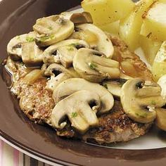 a plate topped with meat covered in mushrooms and potatoes next to some sliced up vegetables