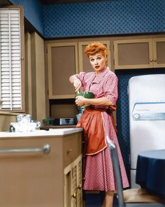 a woman in a red and white checkered dress is holding a green cup while standing next to an oven