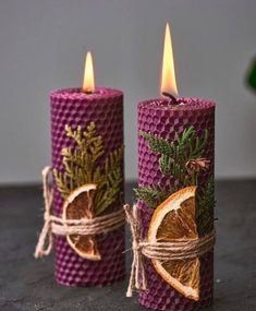 two purple candles with orange slices and pine cones wrapped in twine on top of each other