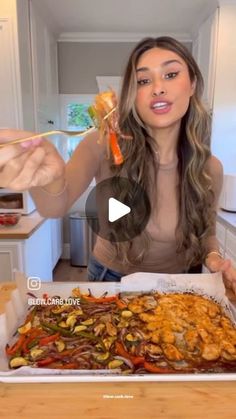 a woman holding a fork and spoon over a tray of food