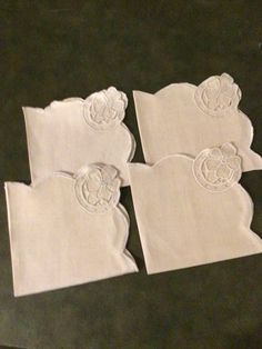 four white napkins with embroidered designs on them sitting next to each other in front of a black table