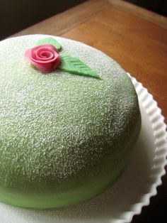 a green frosted cake with a pink rose on top sitting on a white plate