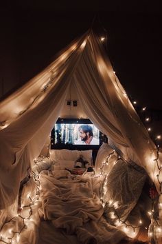 a bed covered in white sheets and lights under a tv screen that is turned on