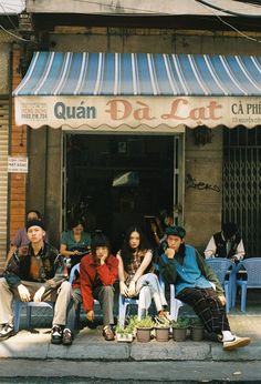 several people sitting on blue chairs in front of a building with an awning over it